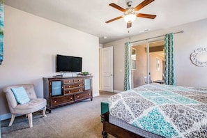 Une chambre à coucher comprenant un lit, une commode, un téléviseur, un ventilateur de plafond et une porte coulissante.