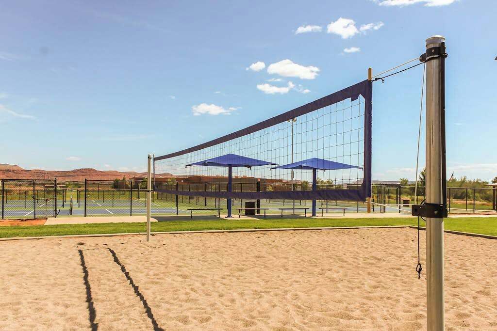 Een volleybalveld met een net, twee blauwe parasols en een metalen paal.