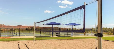 A volleyball court with a net, two blue umbrellas, and a metal pole.