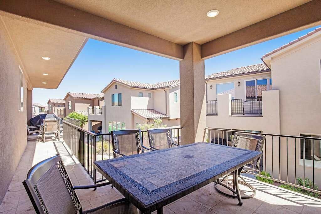 Un patio techado con una mesa y sillas, con vista a una zona residencial con casas.