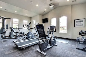 Une salle de sport équipée d’appareils de cardio, de poids libres et d’un téléviseur fixé au mur.
