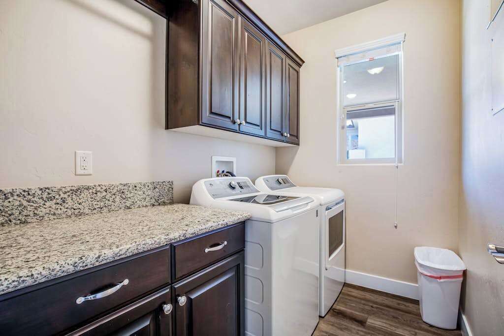 A laundry room with a granite countertop, dark cabinets, and two white washing machines.
