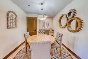 Un comedor con una mesa redonda, cuatro sillas tapizadas, una lámpara de techo y espejos decorativos en la pared.