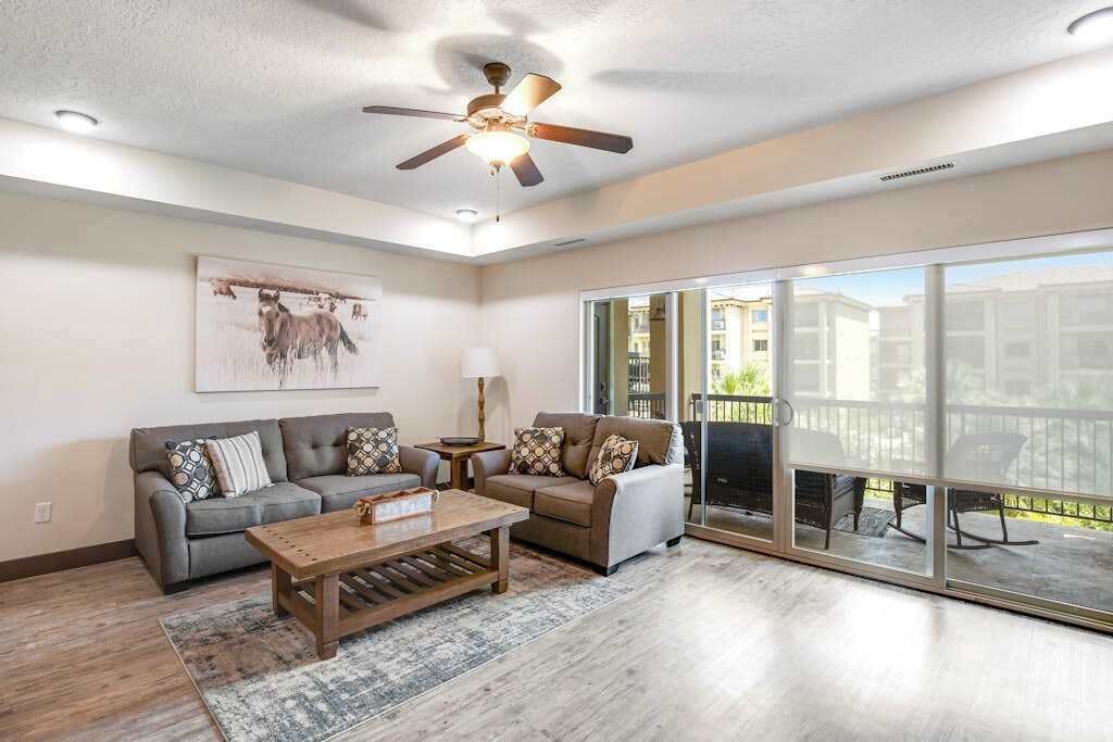 A spacious living room with a ceiling fan, two sofas, a coffee table, and a large sliding glass door leading to an outdoor area.