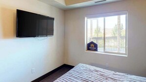Habitación de hotel con una cama, un televisor montado, una ventana con vistas al balcón y un letrero que indica el nombre del establecimiento.
