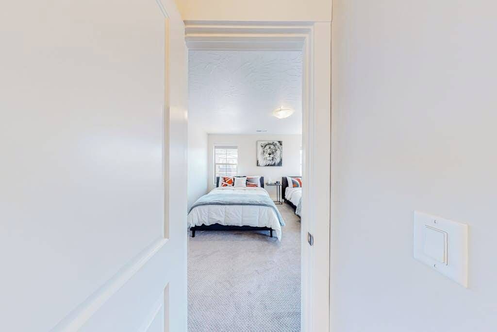 A hallway leading to a bedroom with a bed, a bedside table, and a wall-mounted light fixture.