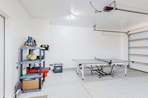 A room with a ping pong table, a shelf with various items, and a trash bin. - 4BR desert townhouse with game room, bikes, & AC (Washington)