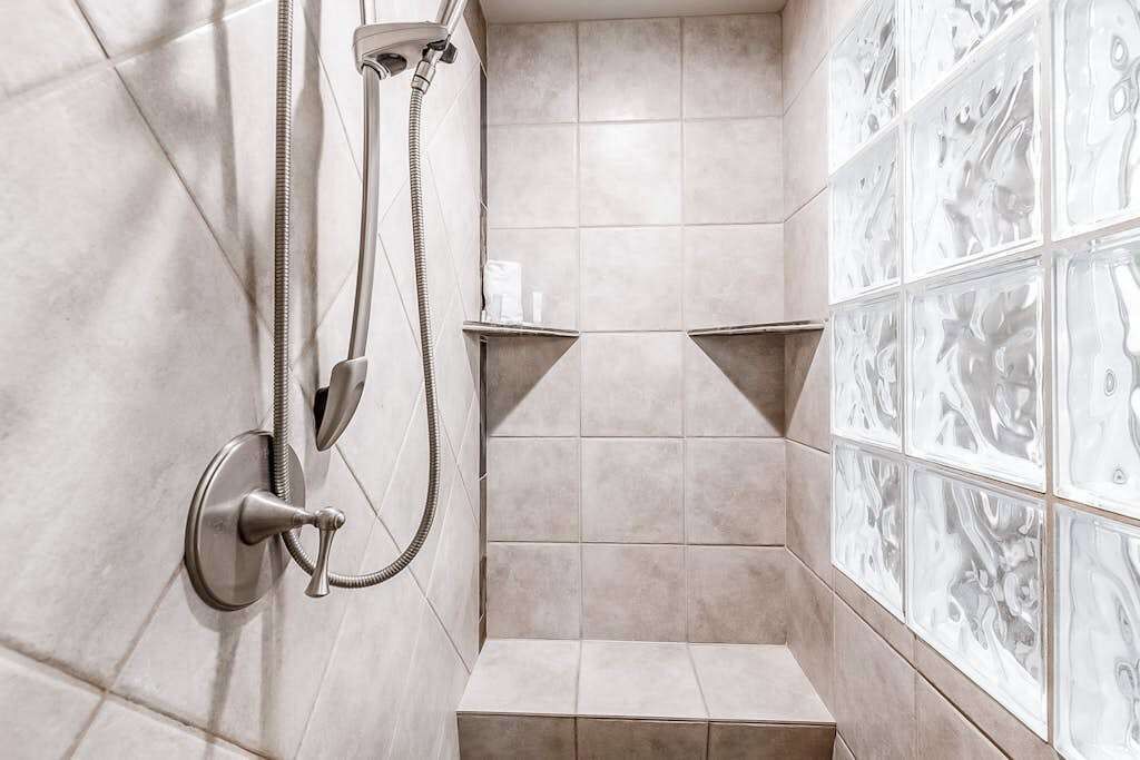 A shower area with a handheld showerhead, a wall-mounted faucet, and a tiled wall with decorative patterns.