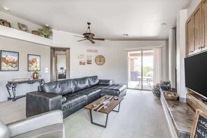 Un salon moderne avec un canapé d’angle, une table basse, un ventilateur de plafond et un grand téléviseur à écran plat.