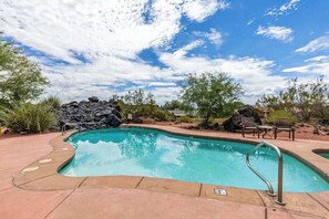 Une piscine agrémentée d’un élément décoratif en pierre, entourée d’une terrasse avec des chaises et une petite table.