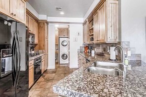A kitchen with wooden cabinets, a stainless steel refrigerator, a built-in oven, a microwave, a washing machine, and a granite countertop with a sink. - 2BR Zion National Park - Hot tub - Pool (Santa Clara)