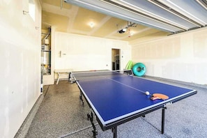 Ein Tischtennistisch mit Ball und Schläger, ein grüner Gymnastikball und eine weiße Tür in einem Raum mit Fliesenboden.