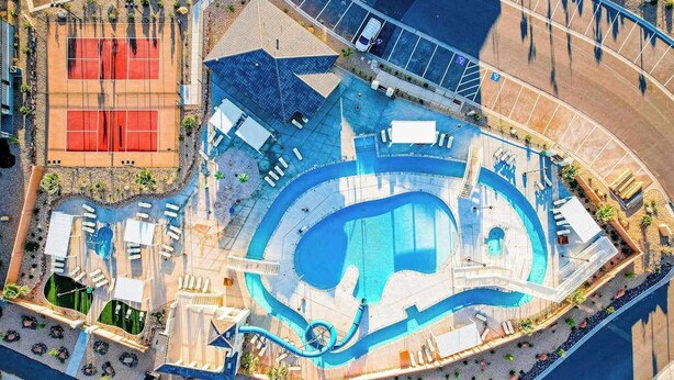 Vista aérea de un resort con una gran piscina, canchas de tenis y tumbonas.
