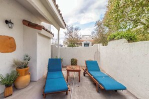 Eine Terrasse mit zwei Lounge-Stühlen und einem kleinen Tisch, umgeben von weißen Wänden und Blumentöpfen.