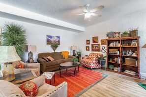 A living room with a sofa, armchair, coffee table, and a bookshelf. - Stylish 1BR Zion National Park - Patio - Pool (St. George)