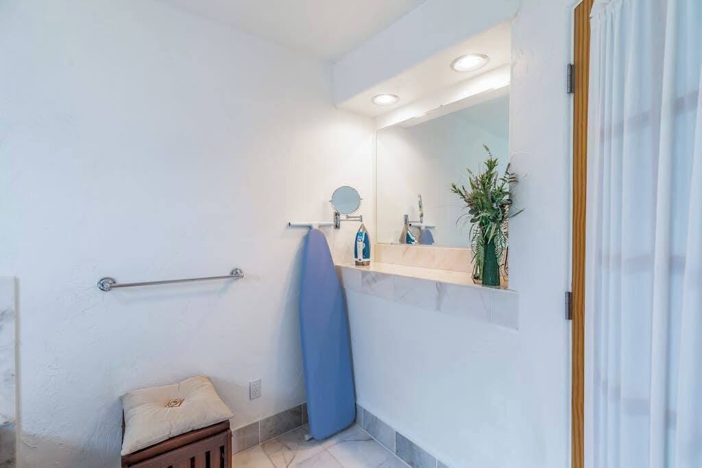 Une salle de bain avec une douche, un porte-serviettes, un lavabo avec un miroir et une plante.