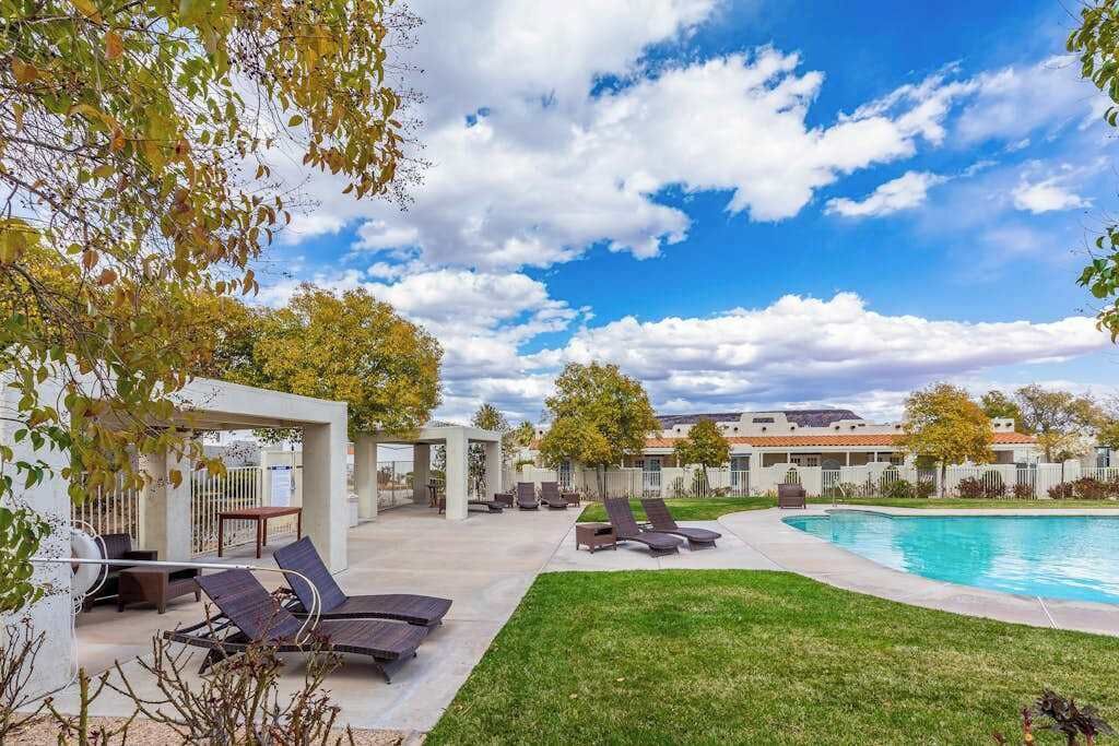 Un espace aménagé au bord de la piscine, avec des chaises longues, un coin salon abrité et une vue dégagée sur un bâtiment situé au loin.