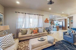 A living room with a sofa, ottoman, and a dining area with a table and chairs. - 3BR home with waterpark and hot tub PV5 (Santa Clara)