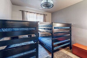 Ein Zimmer mit Etagenbetten, Deckenventilator, einem Vorhangfenster und einer kleinen orangefarbenen Bank.