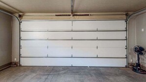 Eine Garage mit geschlossener Tür, einem Ventilator und einer Steckdose an der Wand.