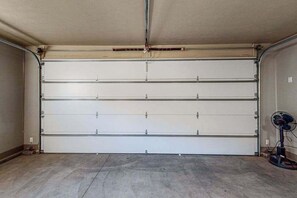 Eine Garage mit geschlossener Tür, einem Ventilator und einer Steckdose an der Wand.
