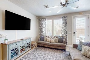 A living room with a sofa, a flat-screen TV, a ceiling fan, and patterned curtains. - Spacious townhome with shared pool & hot tub (Washington)