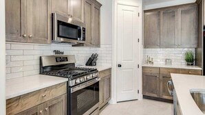 A kitchen with wooden cabinets, a stainless steel stove, a microwave, and a white tiled backsplash. - Brand New 5BR Zion National Park - Patio (Washington)