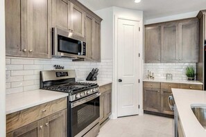 A kitchen with wooden cabinets, a stainless steel stove, a microwave, and a white tiled backsplash. - Brand New 5BR Zion National Park - Patio (Washington)