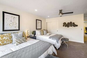 Une chambre avec deux lits, un ventilateur de plafond, des œuvres d’art accrochées aux murs et une porte.