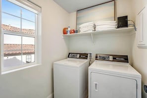 A laundry room with two white washing machines, a window, and a shelf with folded towels and laundry supplies. - Brand New 5BR Zion National Park - Patio (Washington)