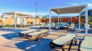 A poolside area with sun loungers and covered seating, surrounded by a brick wall and a clear sky. - Brand New 5BR Zion National Park - Patio (Washington)