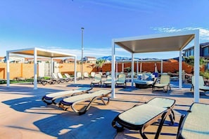 A poolside area with sun loungers and covered seating, surrounded by a brick wall and a clear sky. - Brand New 5BR Zion National Park - Patio (Washington)