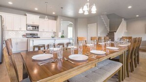 A dining area with a long wooden table set for six, surrounded by chairs, in a modern kitchen with white cabinets and a microwave. - 6BR Spacious townhouse with a pool & lazy river (Hurricane)
