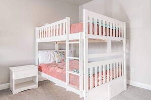 Ein Stockbett mit weißem Gestell, ein Nachttisch und eine rosafarbene Bettdecke.