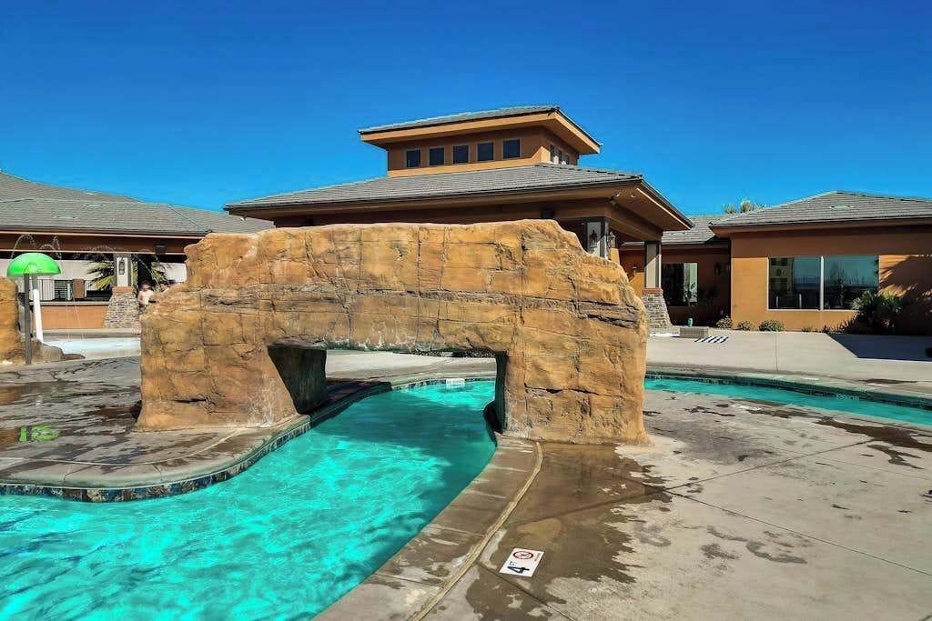A swimming pool with a rock arch structure, clear blue water, and a building with a flat roof in the background.