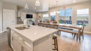 A modern kitchen with a large island, dining area with wooden chairs, and a staircase leading to an upper level. - 6BR Spacious townhouse with a pool & lazy river (Hurricane)