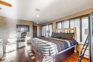 Ein Schlafzimmer mit einem großen Bett, einem Sessel, einem Schreibtisch und einem Fenster mit Jalousien.