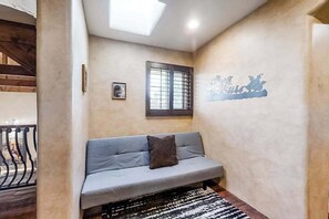 Ein Zimmer mit einer Couch, einem Fenster mit Gitterstäben, einer Wand mit einem Zierfresko und einer Treppe im Hintergrund.