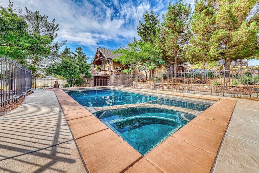 A swimming pool with a wooden deck, surrounded by trees and a fenced area.