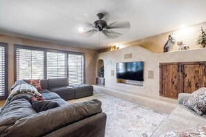 Ein Wohnzimmer mit großem Flachbildfernseher, Deckenventilator und Holzschrank.