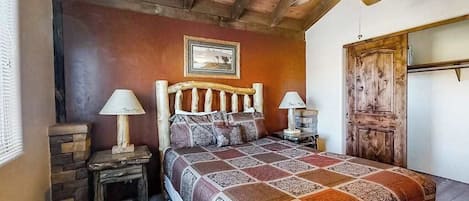 A bedroom with a wooden headboard, a patterned bedspread, two bedside lamps, a rustic door, and a ceiling fan.