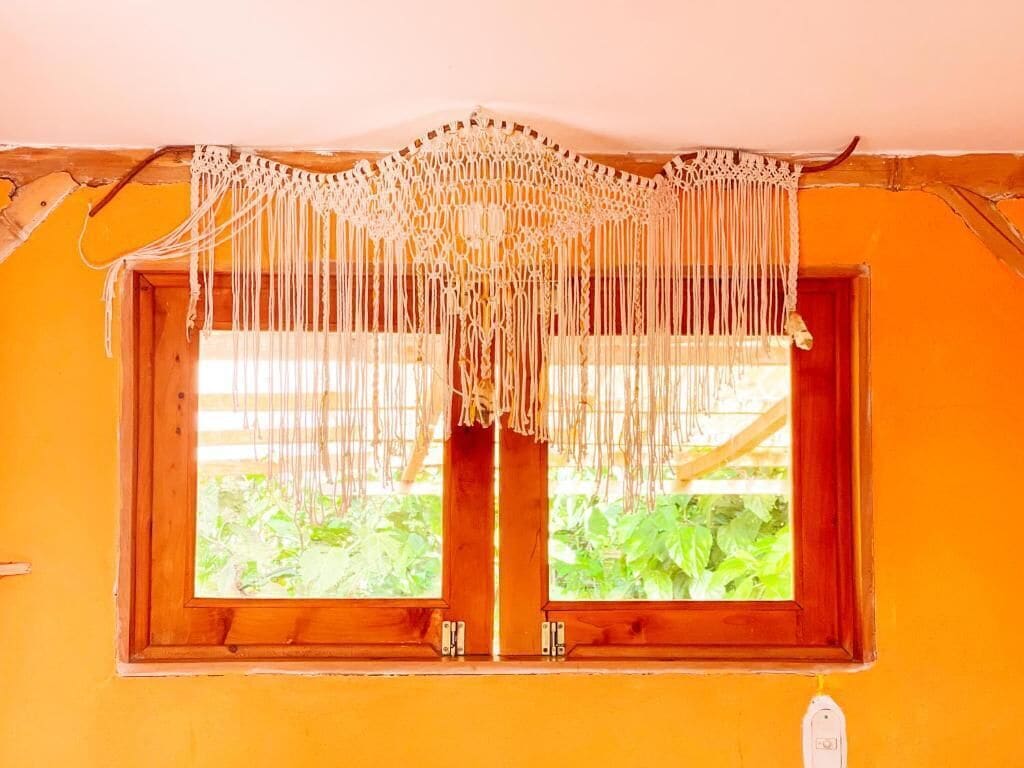 Una ventana con cortina de macramé y un marco de madera.
