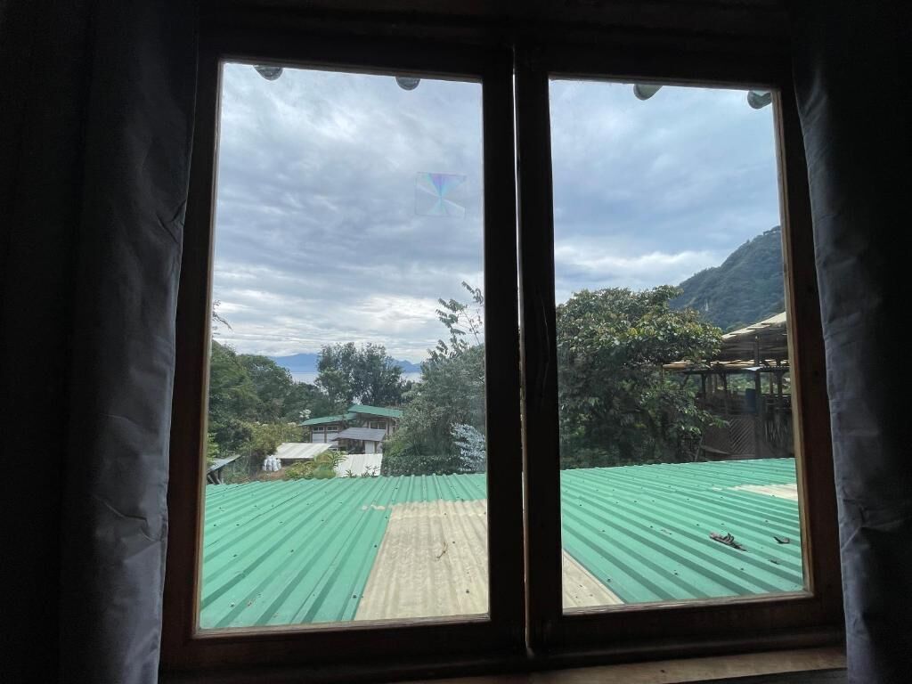 Une pièce dotée d’une grande fenêtre donnant sur un bâtiment dont le toit est végétalisé et sur un paysage montagneux.