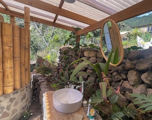 Un baño con pared de piedra, un lavamanos, un espejo y una estructura de madera.