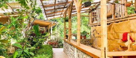 Un jardín cubierto con suelo de piedra, estructuras de bambú y numerosas plantas en macetas.