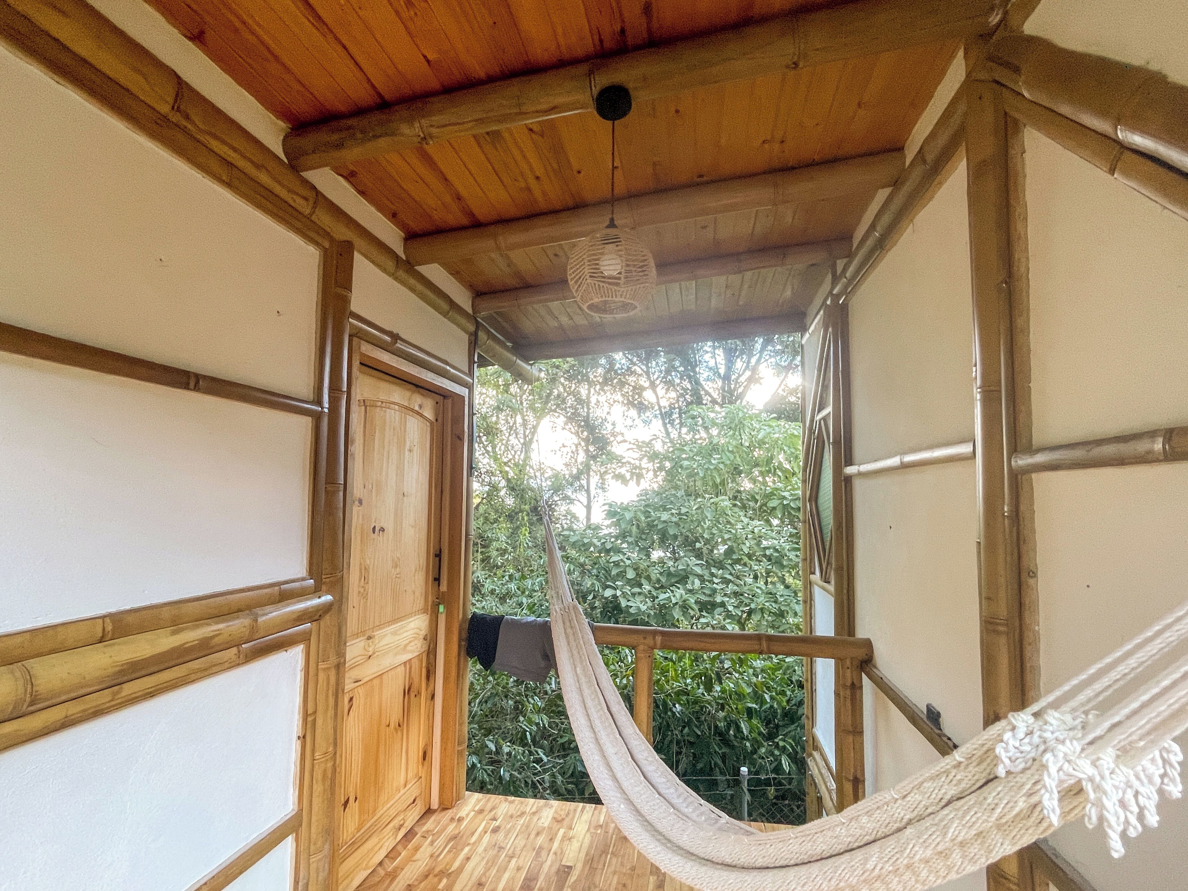 Interior de madeira com rede, uma porta que dá para o exterior e vista para o verde.