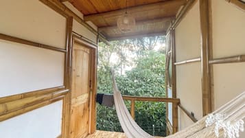 Interior de madeira com rede, uma porta que dá para o exterior e vista para o verde.