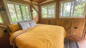Un dormitorio con cama, paredes de madera y ventanas amplias.