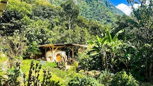 A rustic hut with a thatched roof surrounded by lush greenery and a mountain in the background. - Granja Tzikin (Santa Cruz La Laguna)