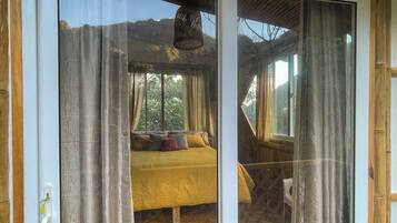 A room with a bed, wooden flooring, and a view of the outdoors.